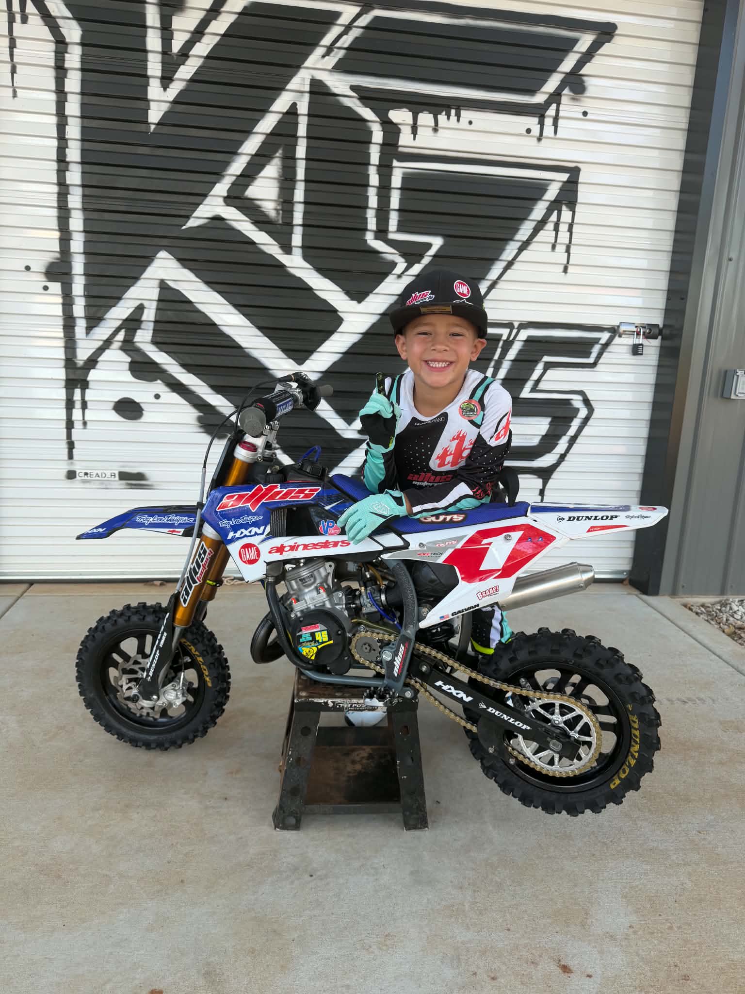 Young rider leaning on his blue number 1 motorcycle — original photograph
